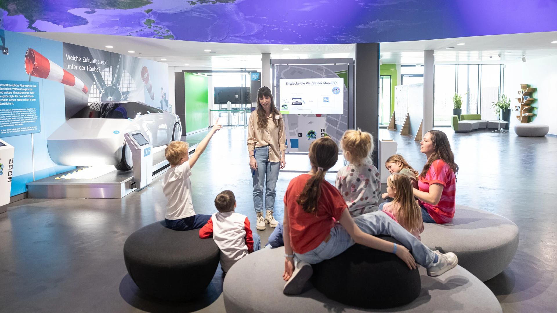 Besucherbetreuerin in Interaktion mit Familie bei F&uuml;hrung in der Innenausstellung.