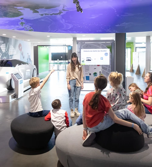 Besucherbetreuerin in Interaktion mit Familie bei F&uuml;hrung in der Innenausstellung.