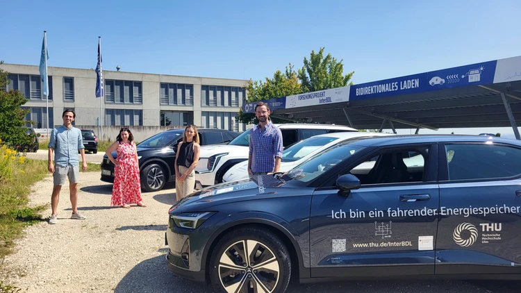 Vier Forschende stehen auf einem Parkplatz bei der Testfahrzeug Flotte.