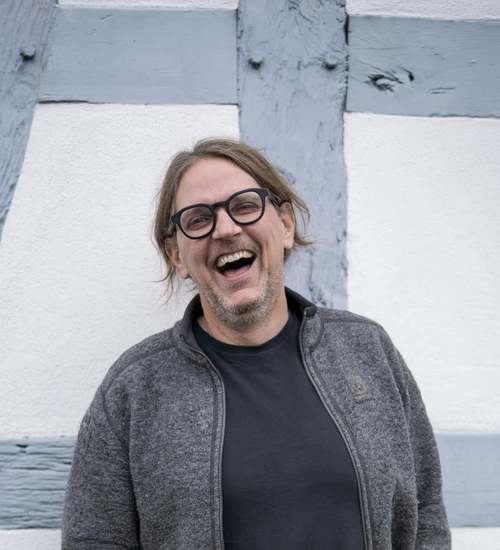 Carsten Herbert, bekannt als Energiesparkommissar, steht lachend vor einer Fachwerkwand.